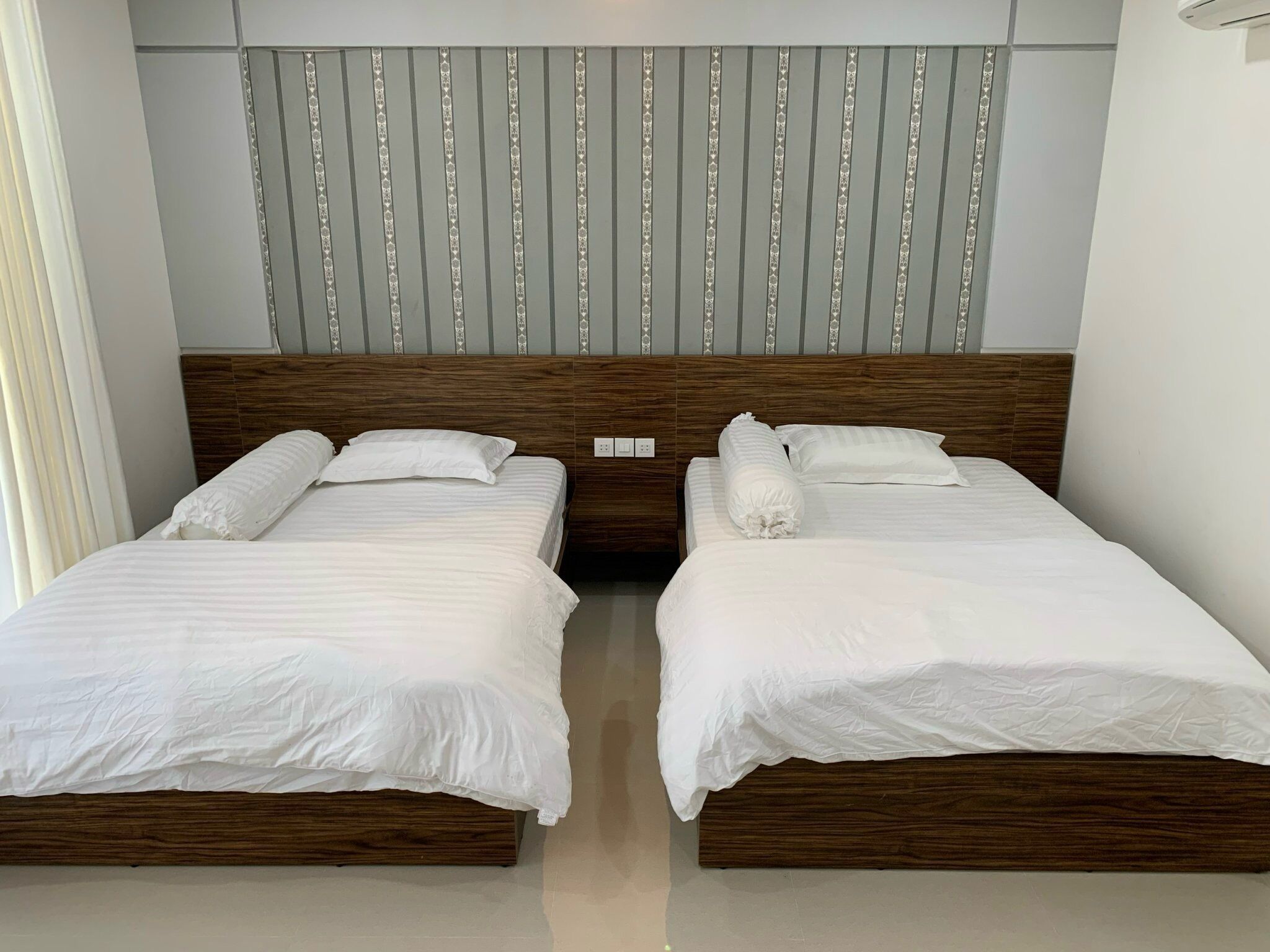 Two neatly made twin beds with wooden headboards and white bedding, arranged in a modern hotel room.
