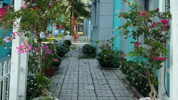 A narrow alleyway with a paved path flanked by white columns and potted plants with pink flowers. - Trang Tien Villas (Phu Quoc)