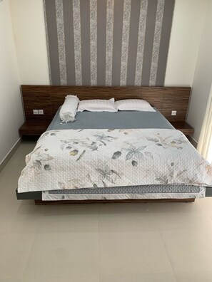 A bed with a floral quilt, a wooden headboard, and a grey-striped curtain. - Trang Tien Villas (Phu Quoc)