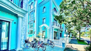 A blue building with a white picket fence, bicycles parked in front, and a cobblestone pathway. - Trang Tien Villas (Phu Quoc)