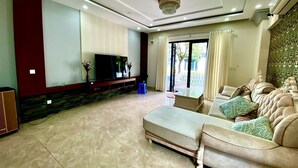 A spacious living room with a large flat-screen TV, a sofa set, and a stone-tiled floor. - Trang Tien Villas (Phu Quoc)