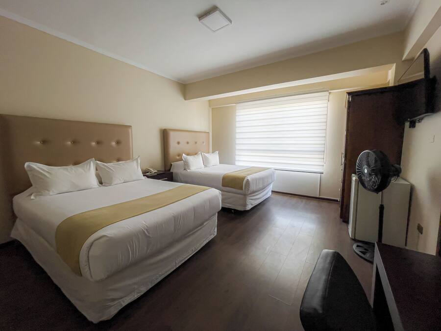 A hotel room with two beds, a desk, a chair, a TV, and a window with blinds.