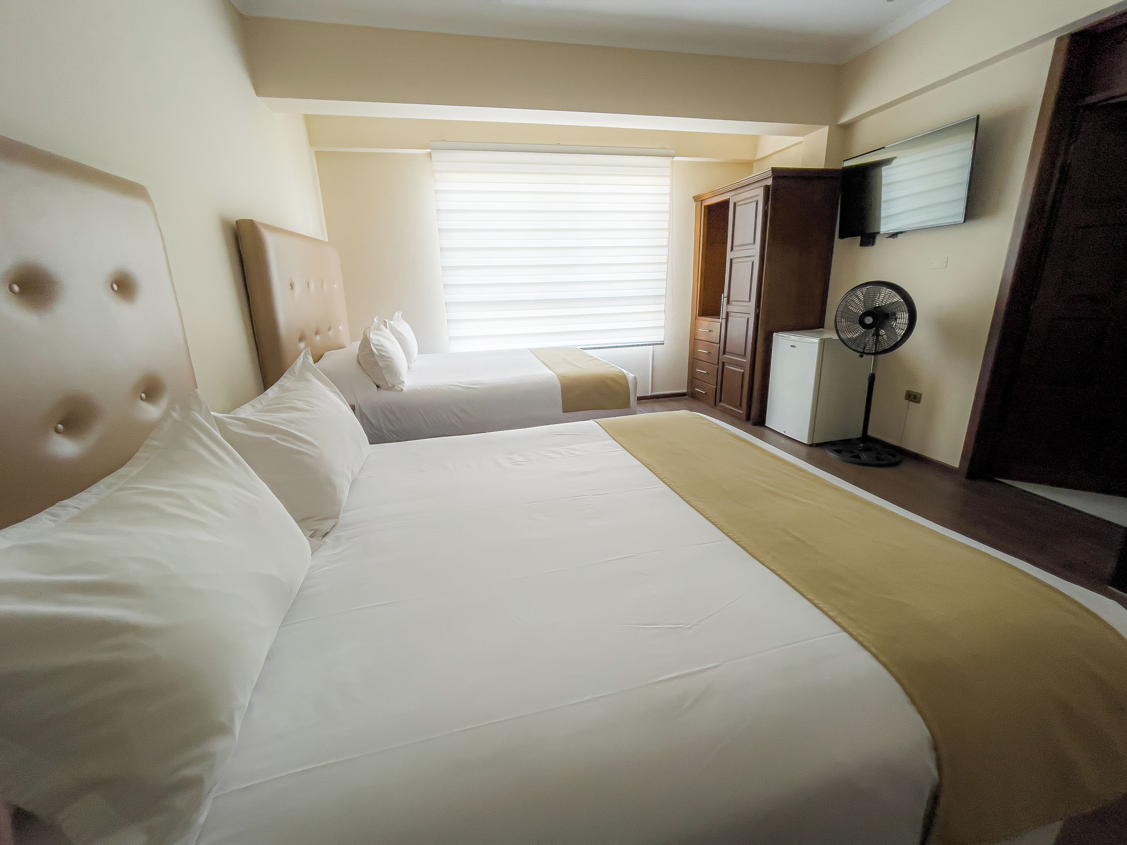 Una habitación de hotel con dos camas, un televisor montado en la pared, un ventilador y un armario.