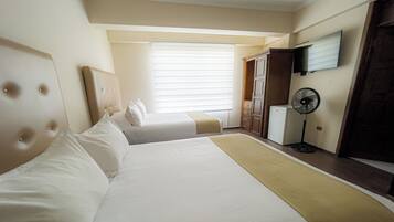 Una habitación de hotel con dos camas, un televisor montado en la pared, un ventilador y un armario.