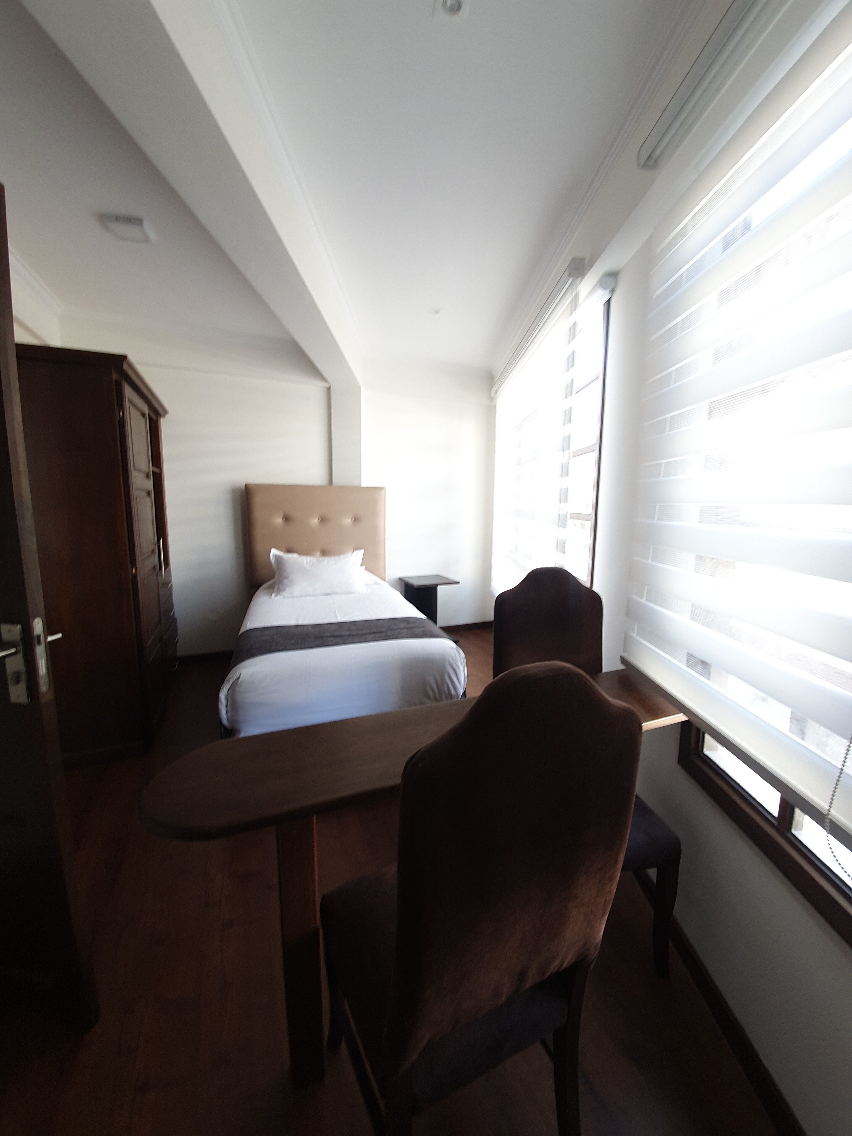 Un dormitorio con una cama, un escritorio de madera, una silla, un armario y una ventana con persianas.