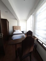 Un dormitorio con una cama, un escritorio de madera, una silla, un armario y una ventana con persianas.