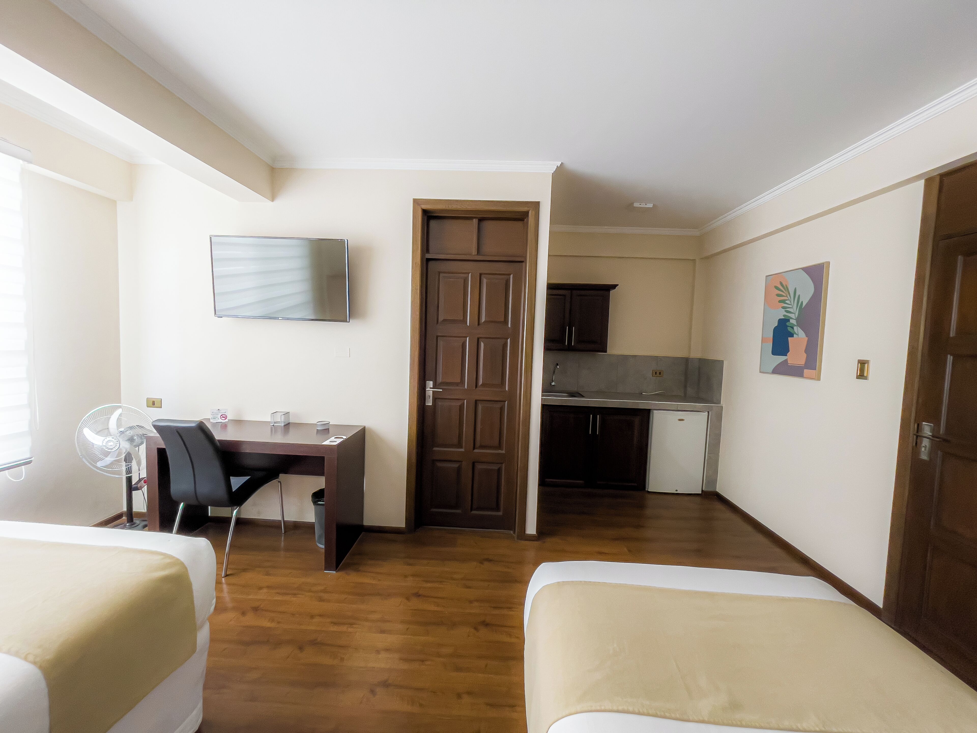 Una habitación pequeña con cama, escritorio, silla, televisor y kitchenette.