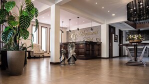 Eine geräumige Lobby mit einer Rezeption, großen Topfpflanzen und einem Chandelier.