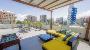 Eine Dachterrasse mit gelber Sitzgelegenheit, einem Kicker und Kübelpflanzen.