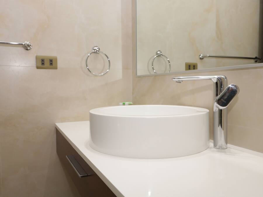 Un baño moderno con un lavabo blanco redondo, grifo cromado y un espejo encima.