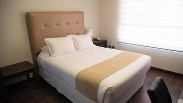 Un letto rifatto con una testiera, un comodino, una lampada e una finestra con tende.