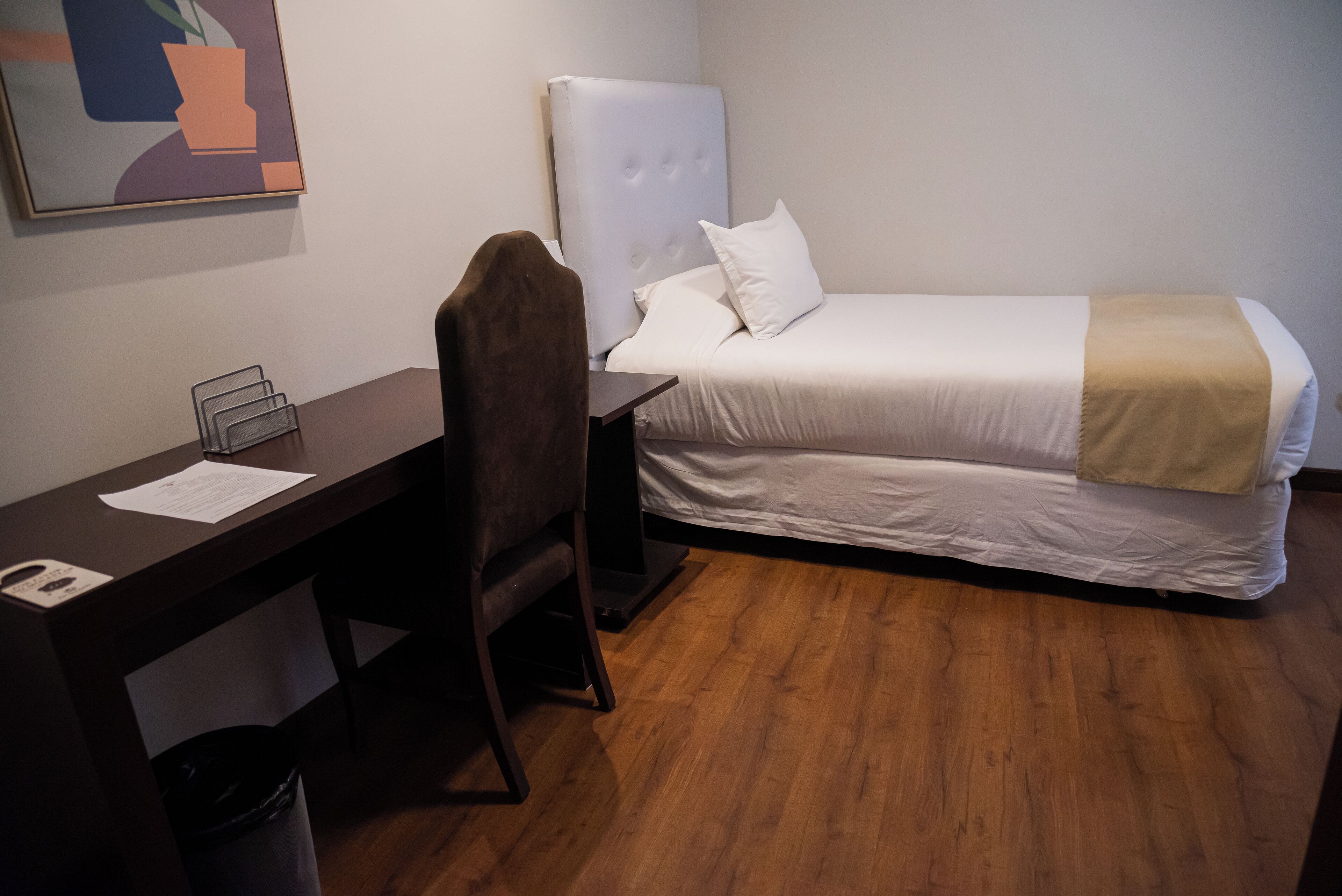 Et hotelværelse med seng, skrivebord, stol og skraldespand.