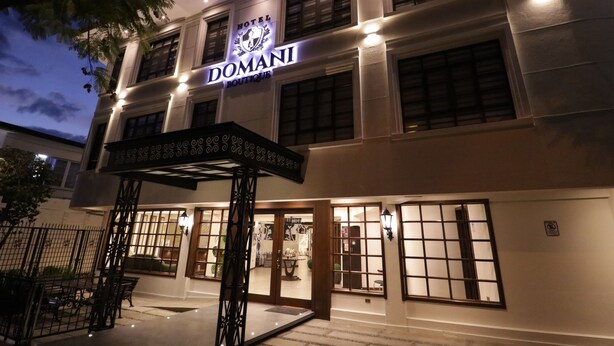 Ein Hotel mit einem Schild, auf dem 'DOMANI BOUTIQUE HOTEL' steht, und einem überdachten Eingangsbereich.