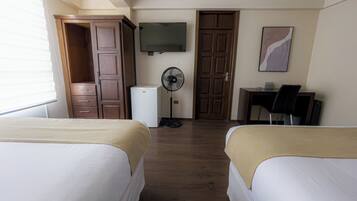 Habitación de hotel con dos camas, televisión, ventilador, escritorio con silla y armario.
