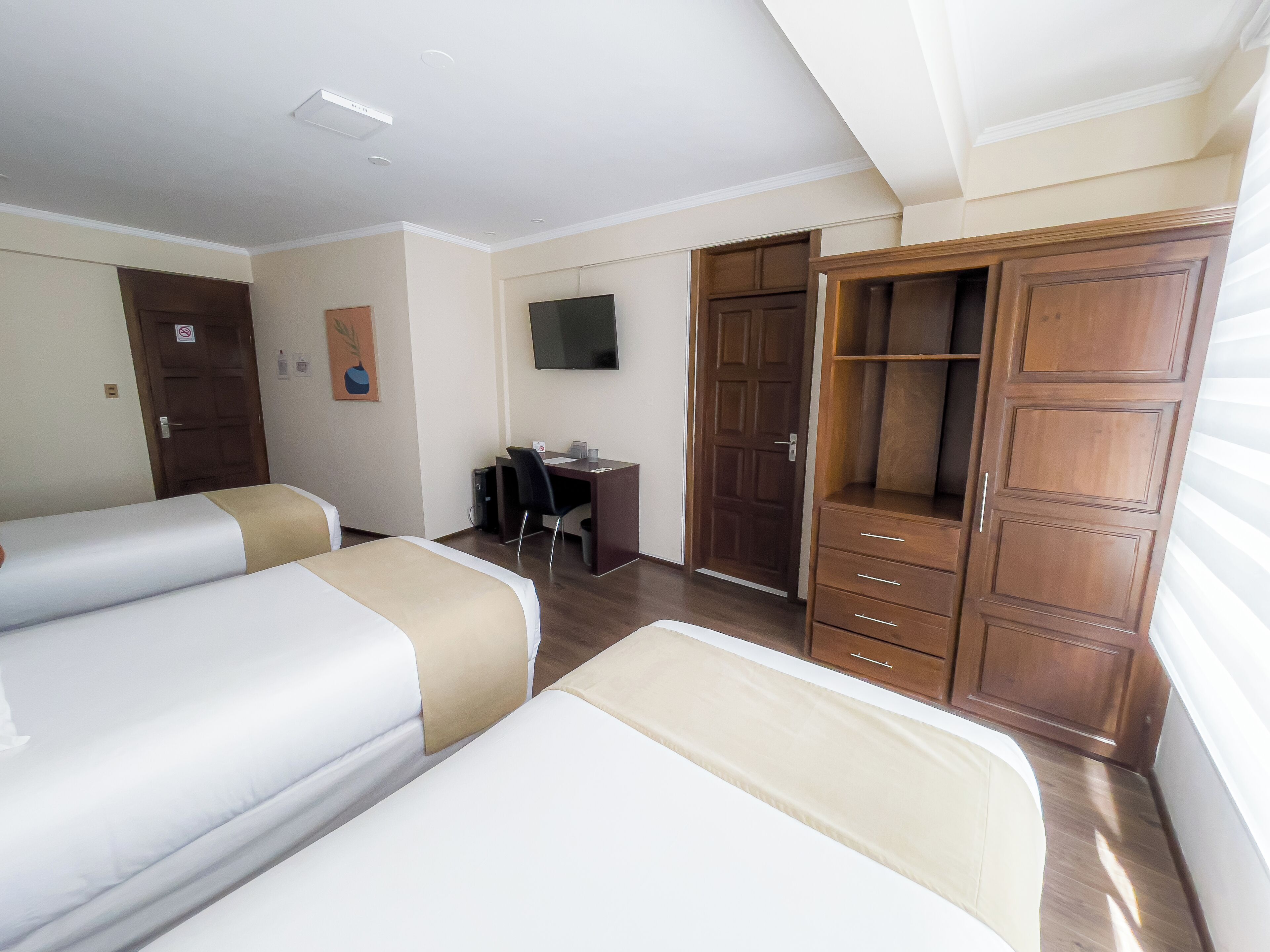 A hotel room with two beds, a desk, a TV, and a wardrobe.