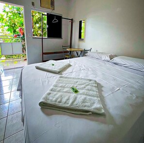 A hotel room with a bed, two towels, a chair, a small table, and a window with a view of greenery.