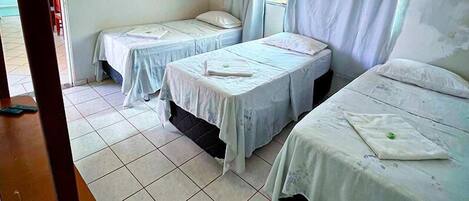 Una habitación con tres camas individuales, suelo de baldosas y una ventana con cortinas.