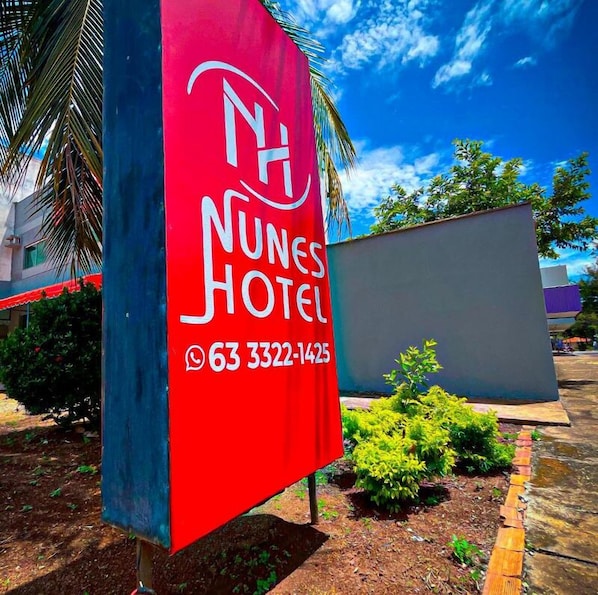 A red and blue hotel sign with the name 'Nunes Hotel' and a phone number.