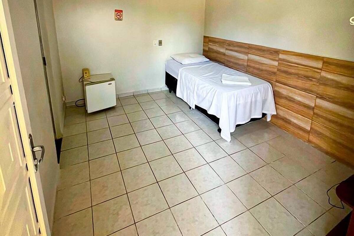 Une petite pièce propre, avec un lit, un petit bureau et un sol carrelé.