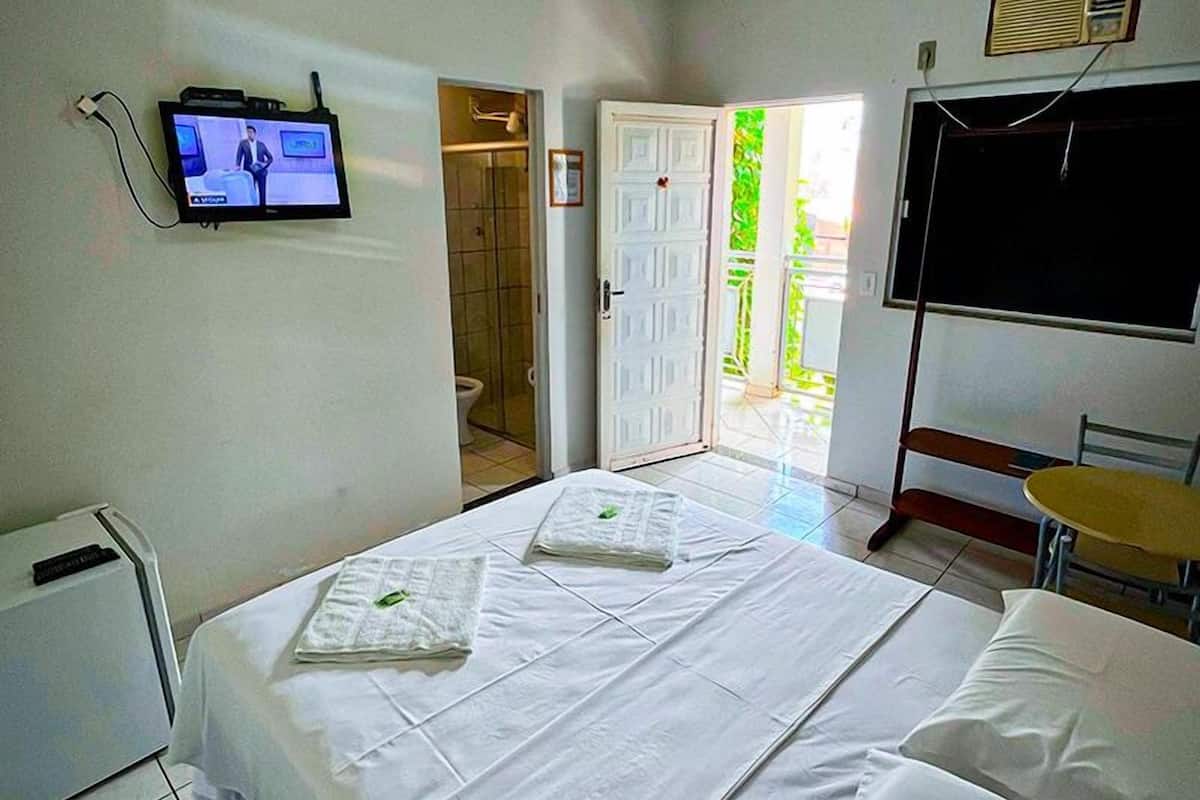 Une chambre d’hôtel équipée d’un lit, d’une télévision, d’un bureau et d’une fenêtre donnant sur un paysage verdoyant.