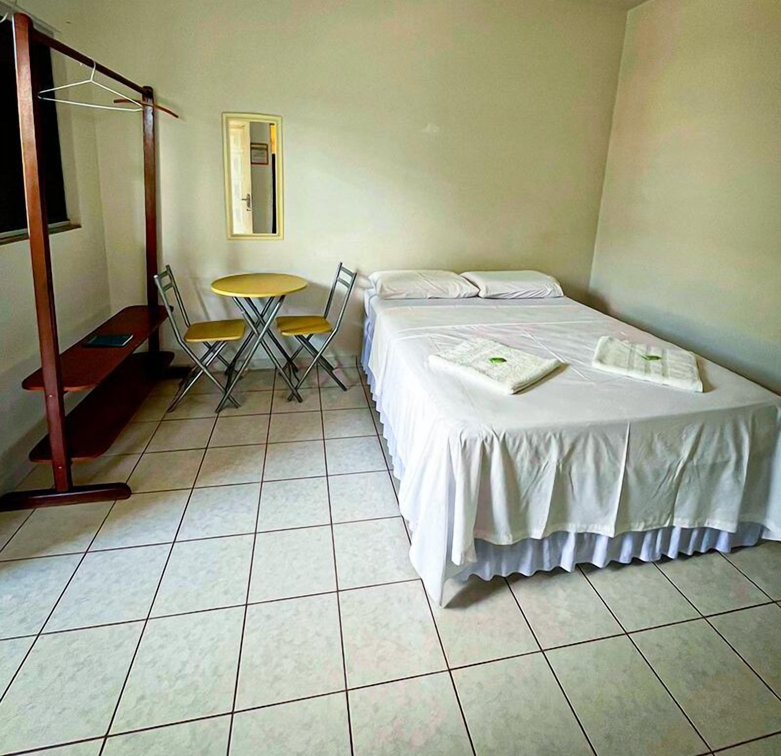A room with a bed, a small table with chairs, a hanging clothes rack, and a mirror on the wall.