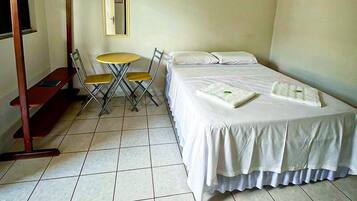 Una habitación con una cama, una pequeña mesa con sillas, un perchero y un espejo en la pared.