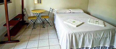 A room with a bed, a small table with chairs, a hanging clothes rack, and a mirror on the wall.