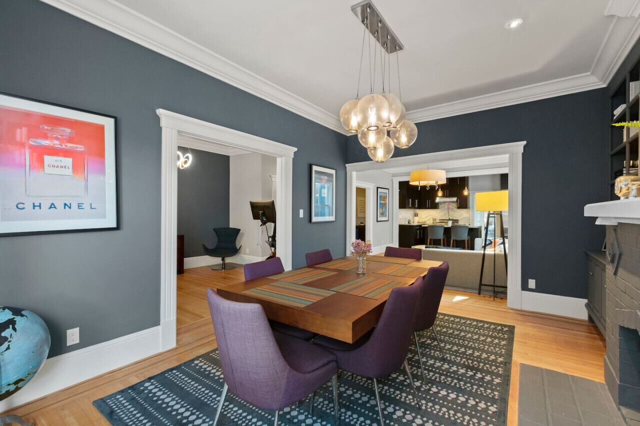 A modern dining room with a wooden table, purple chairs, and a chandelier.