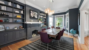 Une salle à manger moderne avec un mur gris foncé, une cheminée, une grande table à manger entourée de chaises violettes et un tapis à motifs noir et blanc.