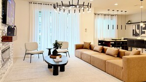A modern living room with a sofa, chairs, a coffee table, and a TV mounted on a brick wall. - Luxe Orlando Villa - Game Room, Pool, Resort Amenities Near Disney (Four Corners)