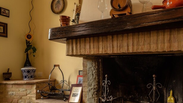 A rustic fireplace with a stone mantle, a wooden shelf above holding a vase, a candle holder, and a wine glass.