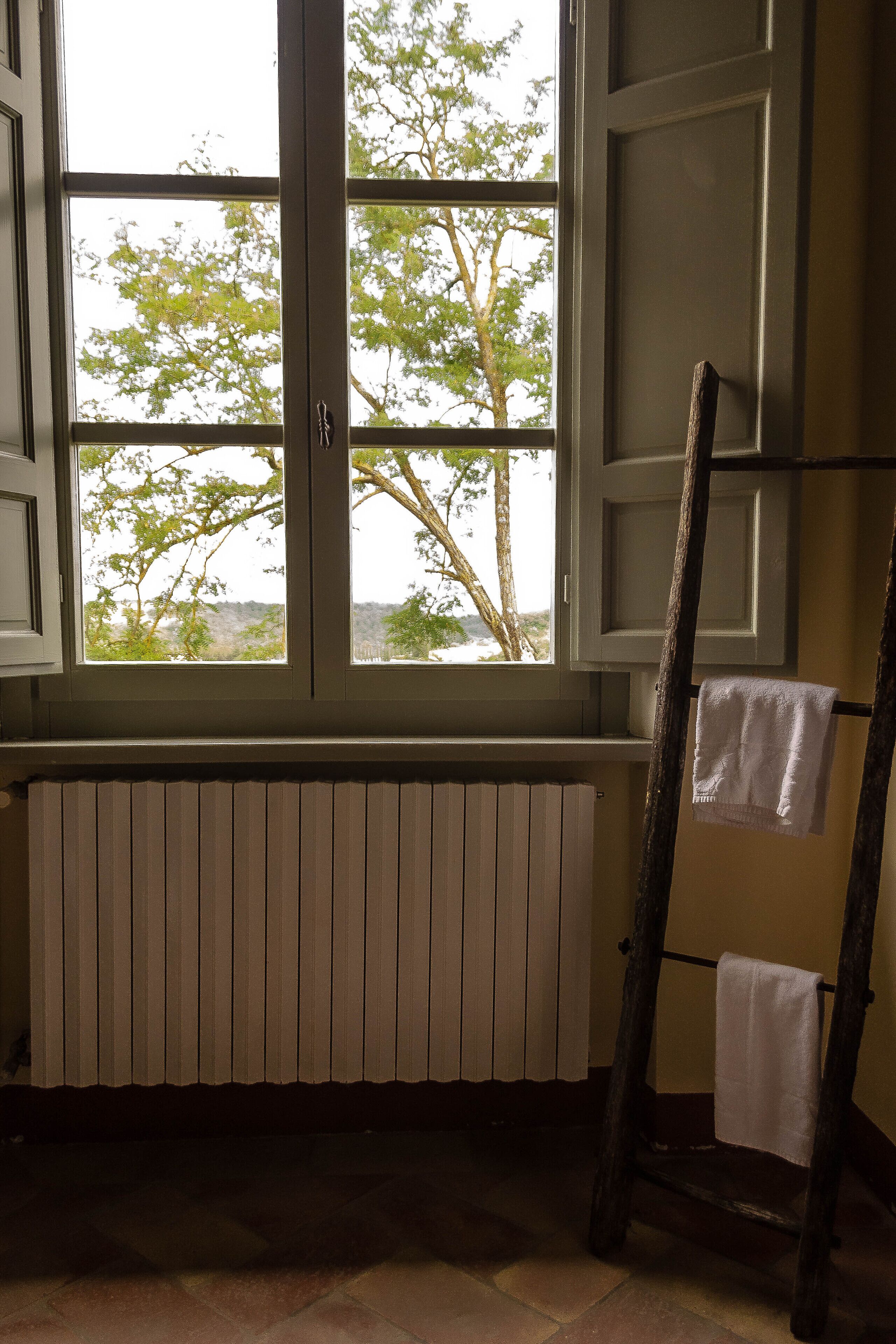 Una habitación con ventana, un radiador y una escalera de madera apoyada en la pared.