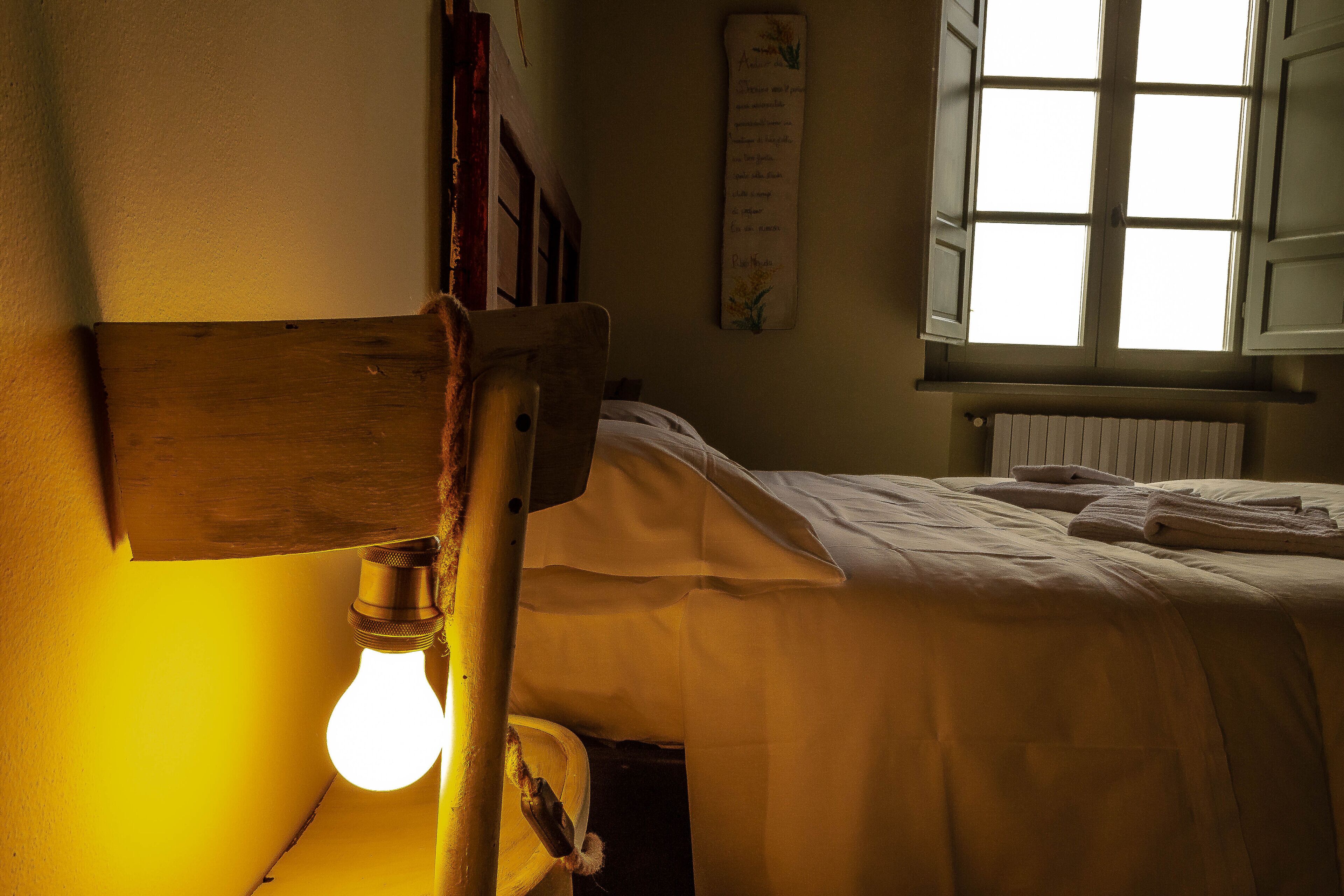 A bedroom with a wooden headboard, a bedside lamp, a window with shutters, and a radiator.