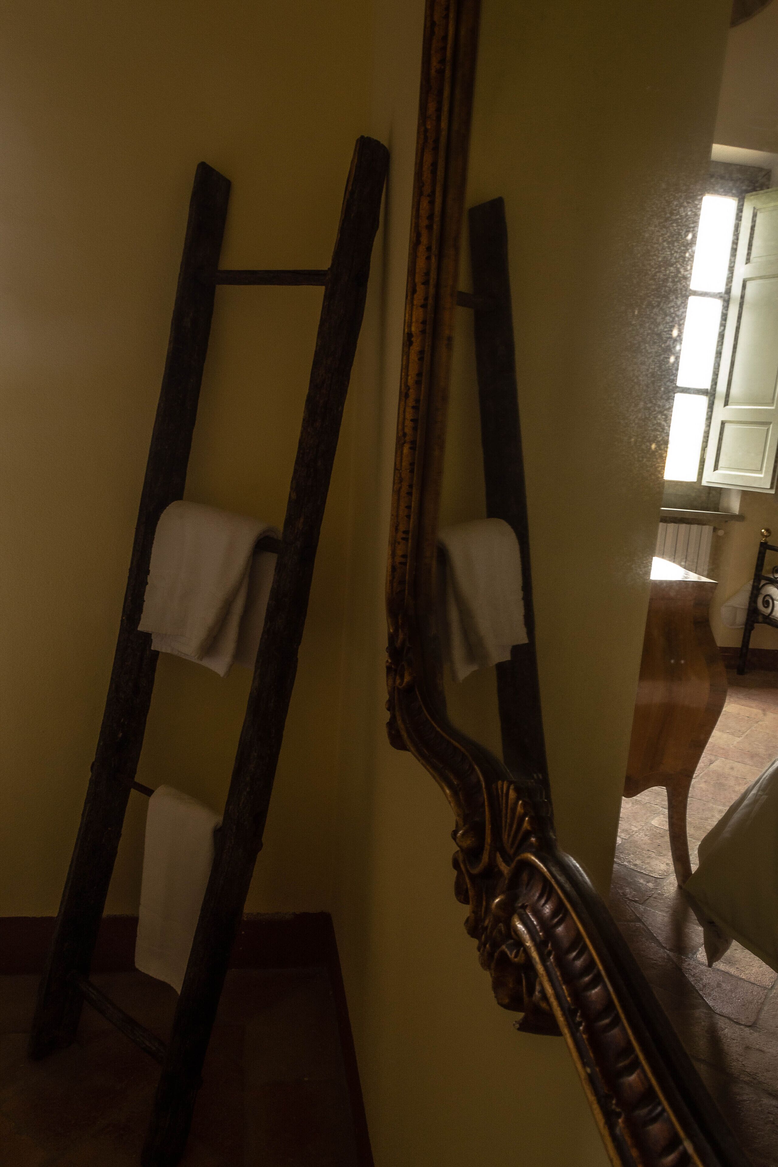 A mirror with a wooden frame leaning against a wall, a towel hanging on the mirror, and a glimpse of a kitchen area in the background.