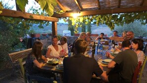 A group of people dining at an outdoor table with a pergola overhead, surrounded by greenery.
