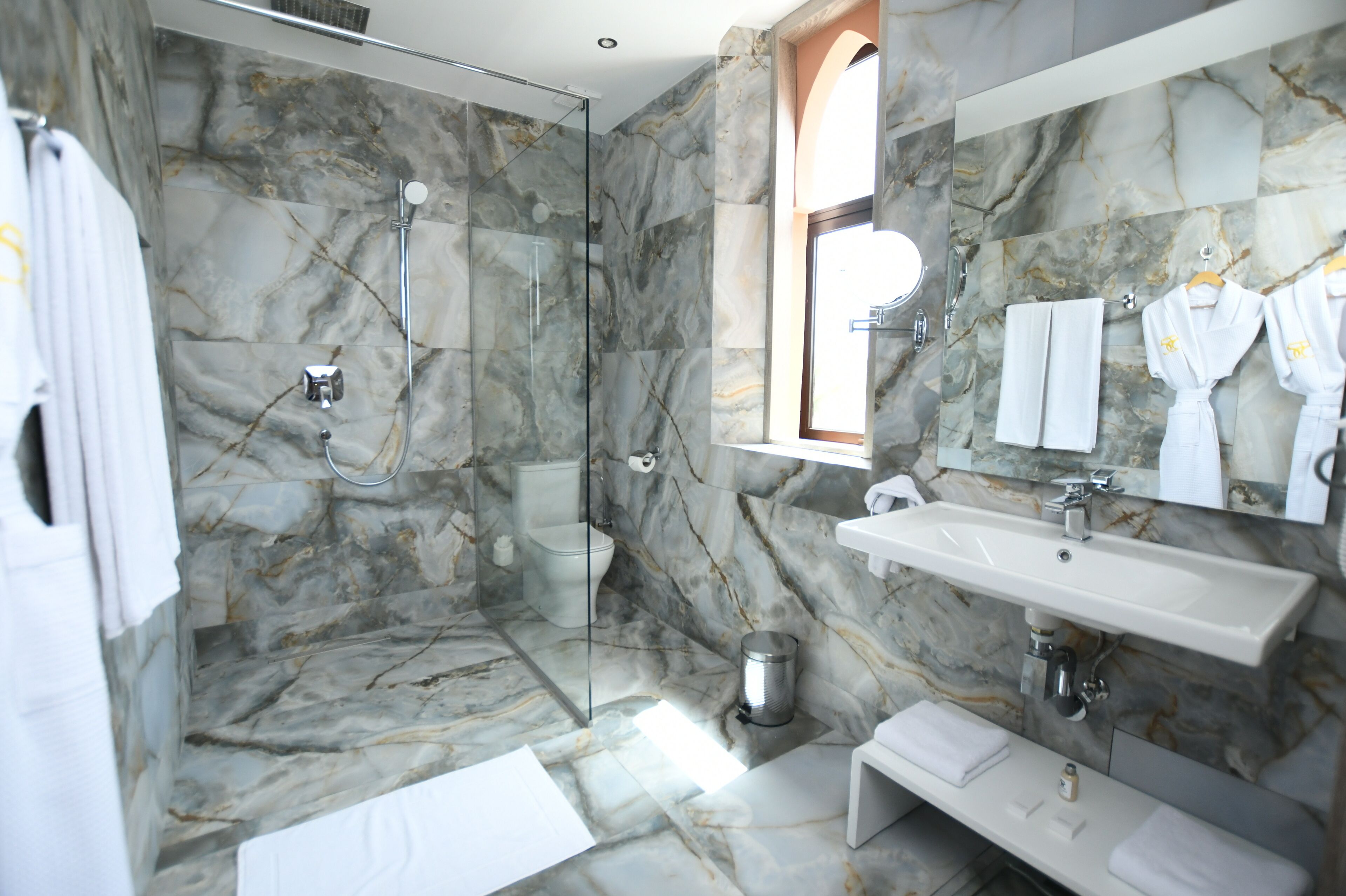 A modern bathroom with a glass-enclosed shower, marble walls, a large mirror, and a white sink.