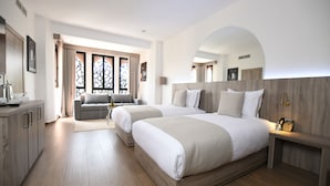 Une chambre d’hôtel moderne avec deux lits, un canapé, un bureau et une grande fenêtre avec des rideaux.