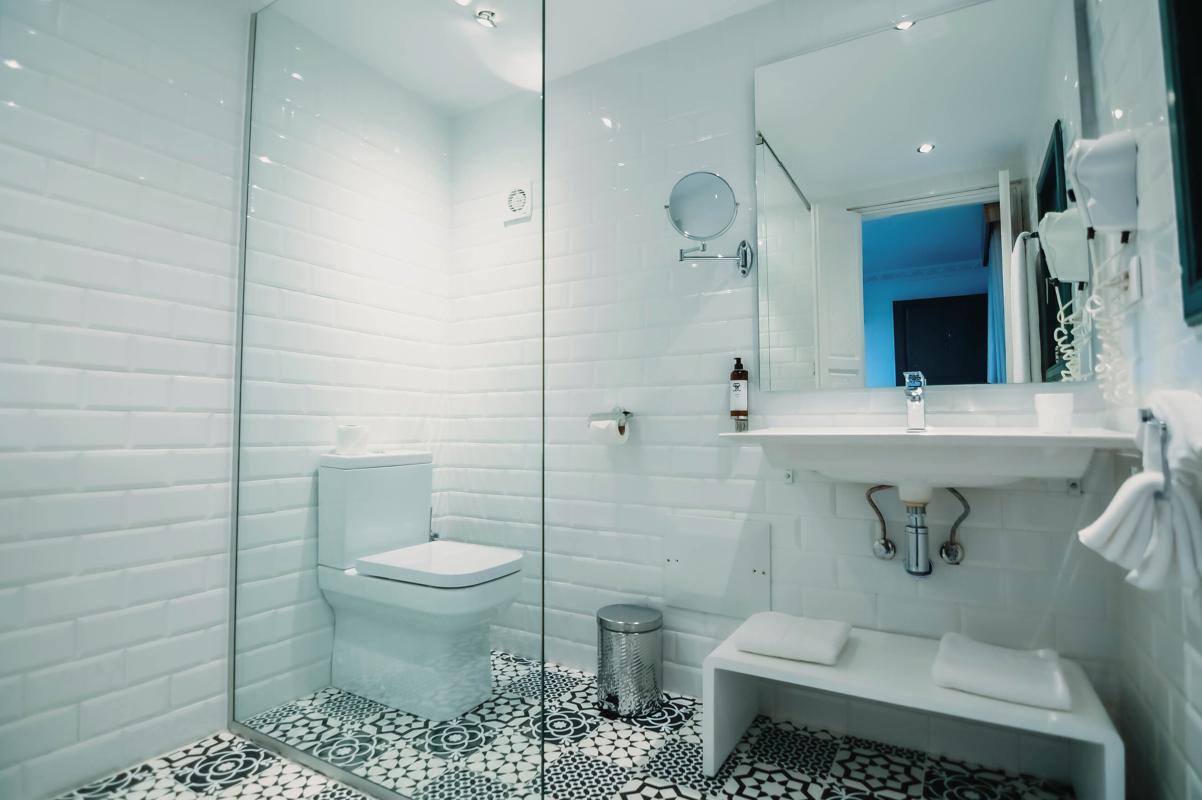 A modern bathroom with a glass shower enclosure, white tiles, and a patterned floor.