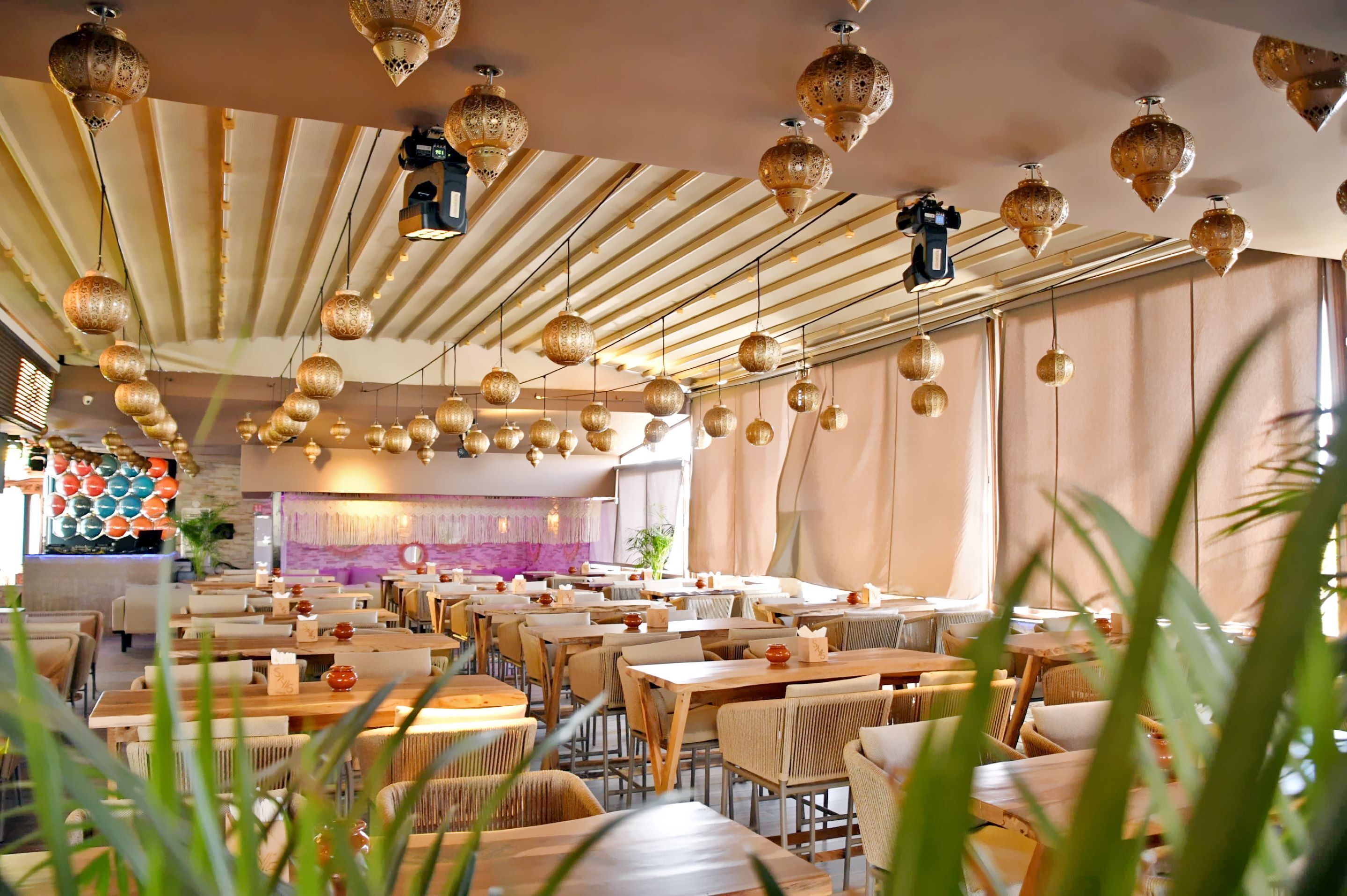 Un restaurante con varias mesas y sillas, faroles colgantes y un ventanal grande.