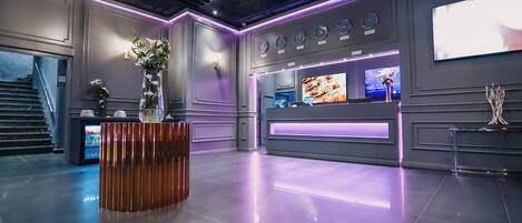 A modern lobby with a reception desk, a decorative vase, a wall-mounted clock, and a television screen.