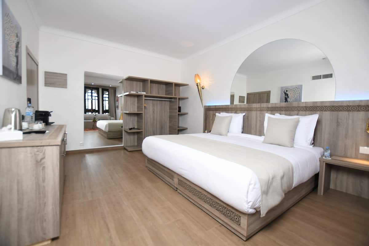 A modern hotel room with a large bed, wooden furniture, and a built-in wardrobe.