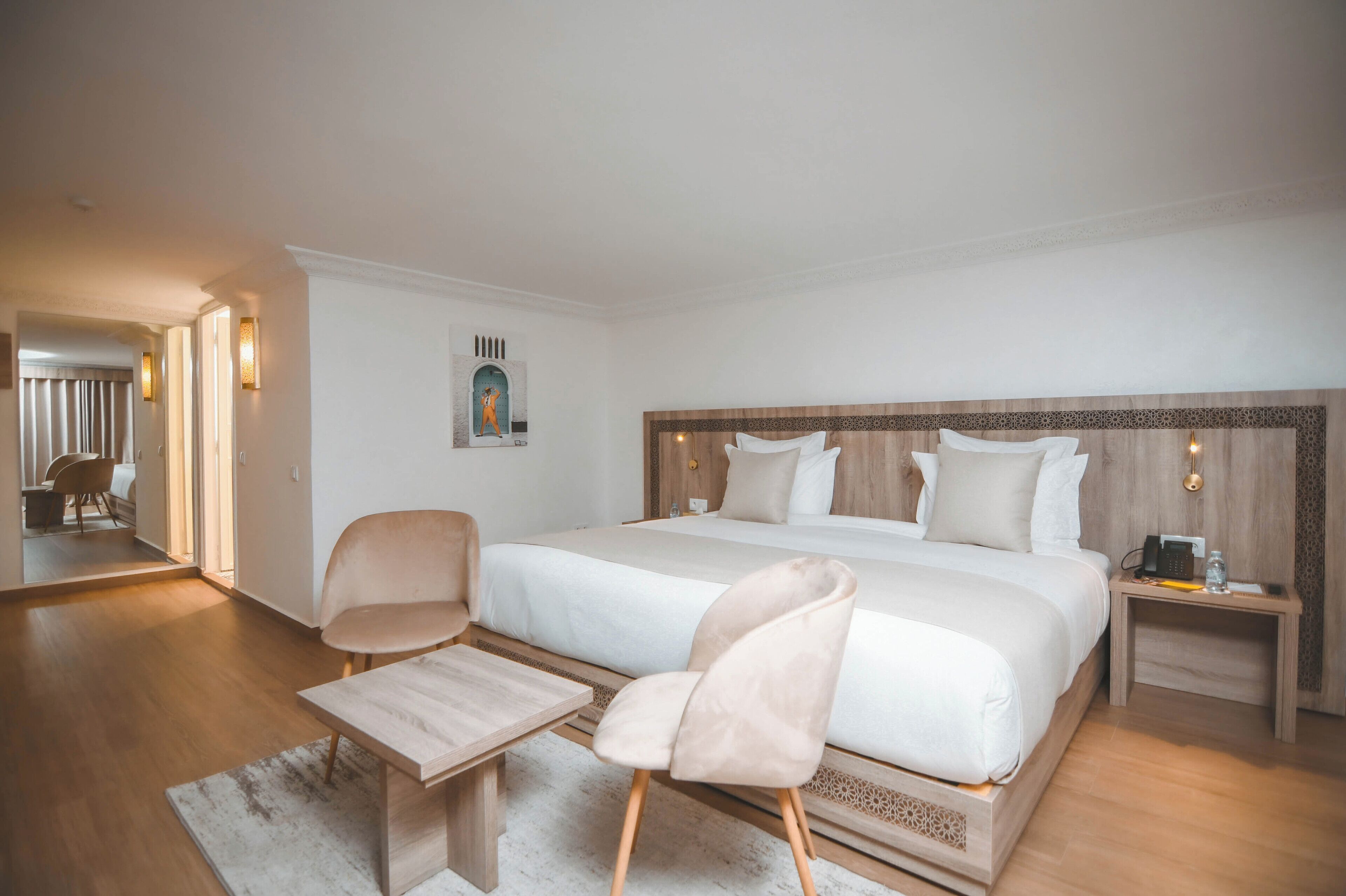 A modern hotel room with a large bed, two bedside tables, a chair, and a small table.