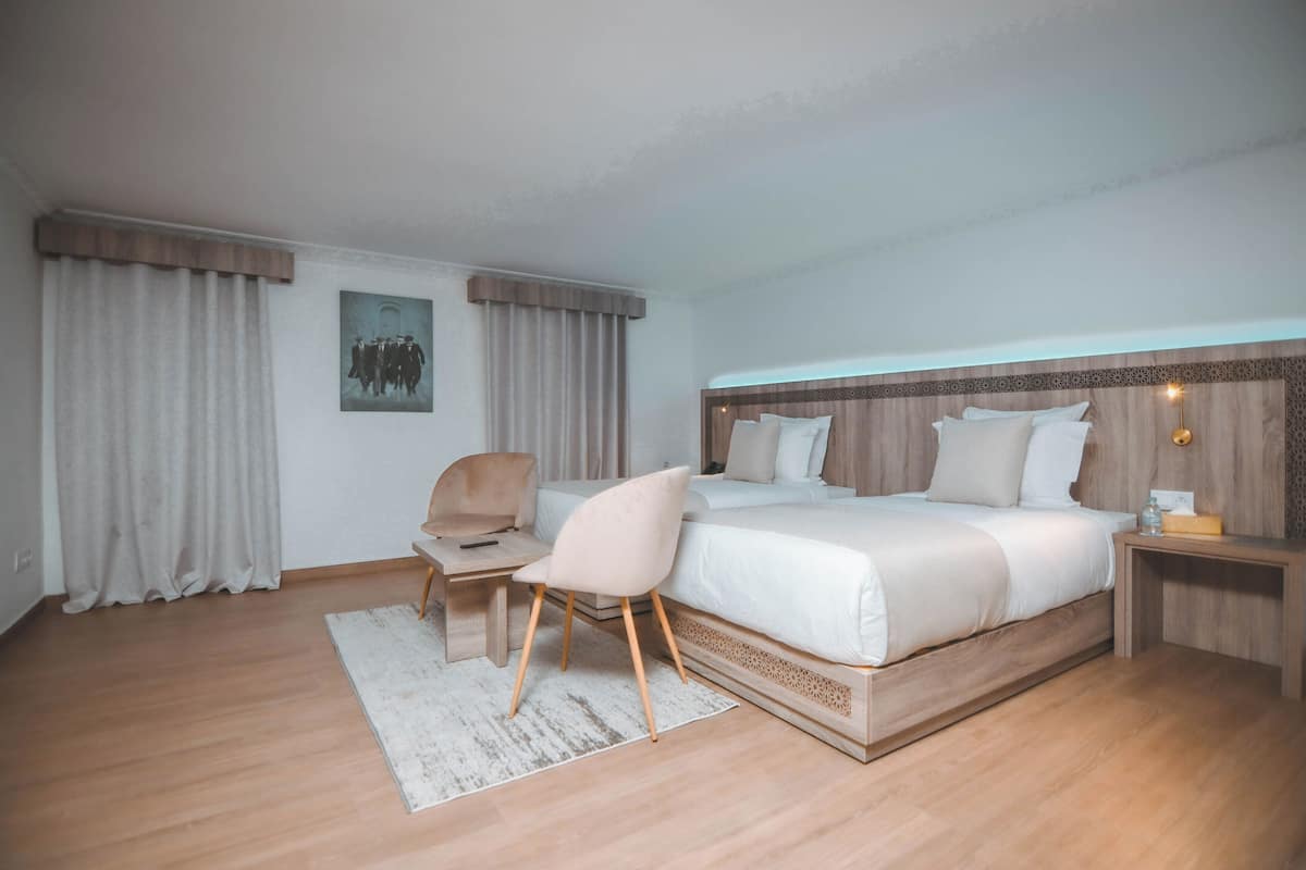 A modern hotel room with a large bed, a desk, a chair, and a nightstand.