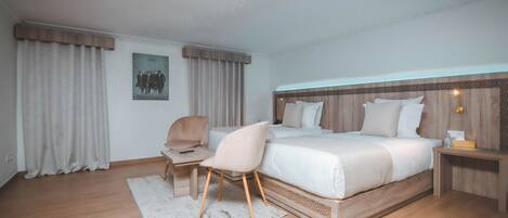 A modern hotel room with a large bed, a desk, a chair, and a nightstand.