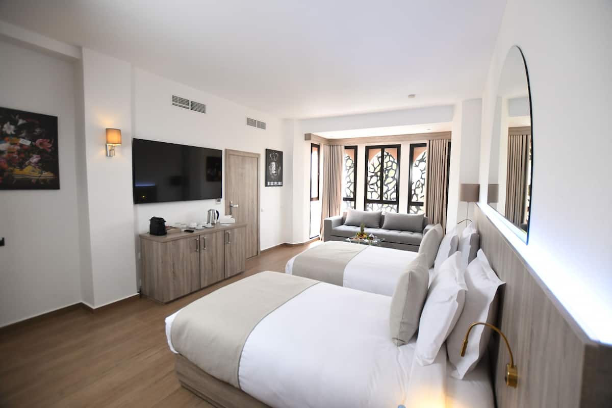 A hotel room with two beds, a TV, a desk with a lamp, and a window with curtains.