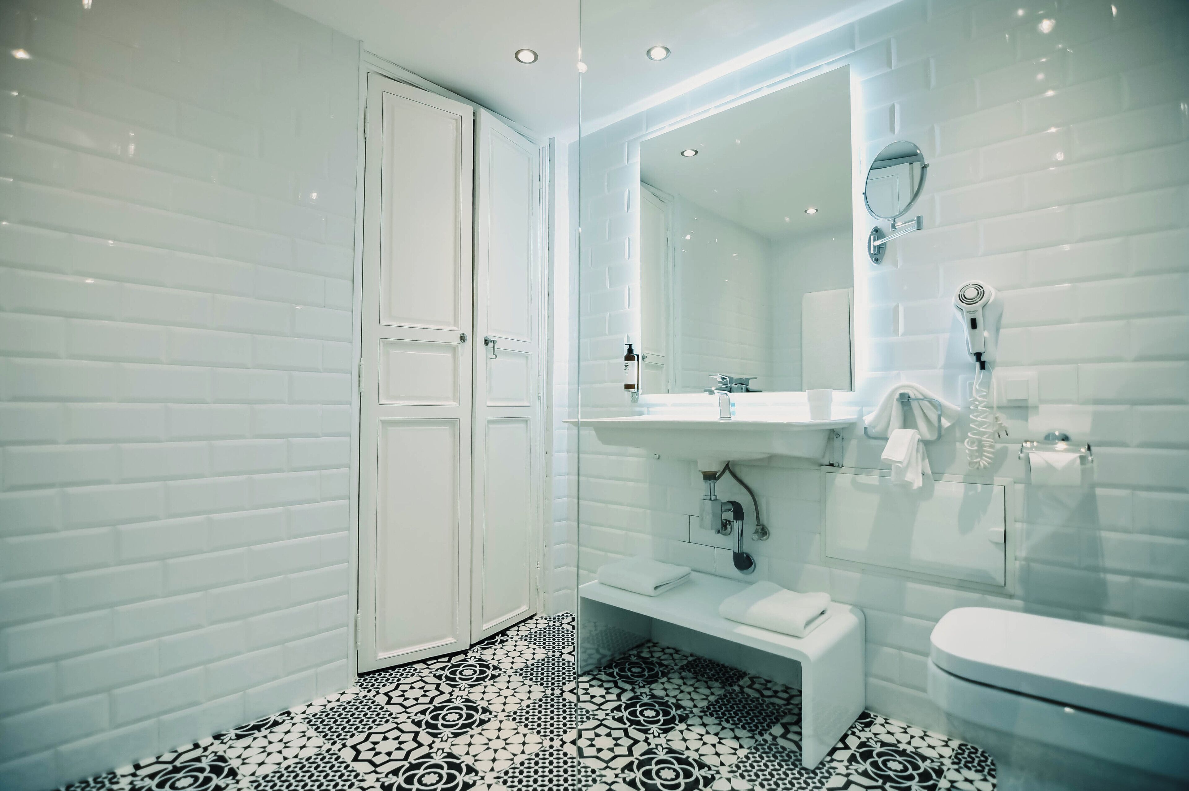 A modern bathroom with white tiled walls, a glass shower enclosure, a white sink, and a toilet.