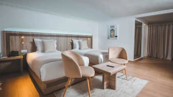 Une chambre d’hôtel avec deux lits, une petite table, deux chaises, une table de chevet et une lampe fixée au mur.
