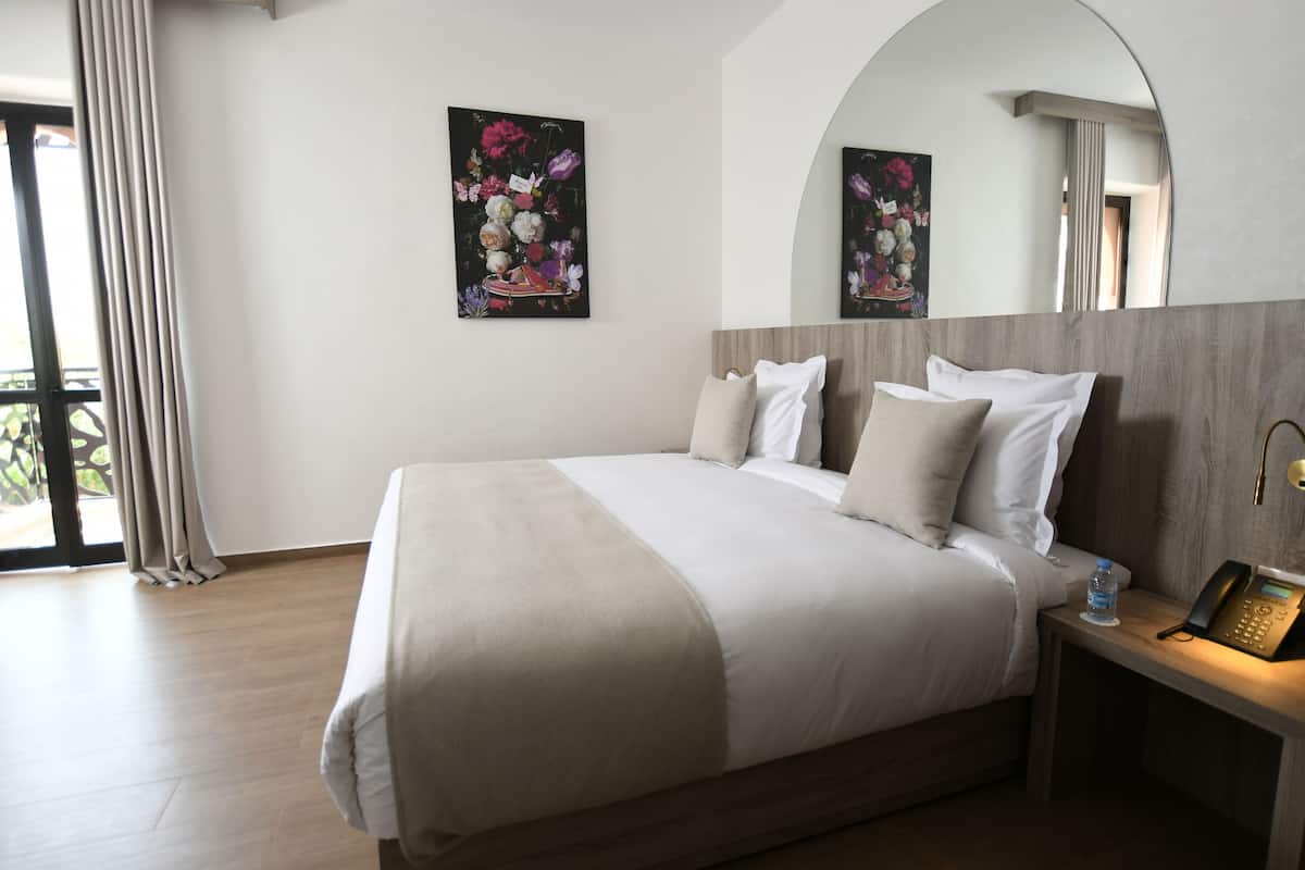 A hotel room with a large bed, a bedside table with a phone, and a painting on the wall.