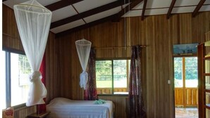 Een kamer met twee bedden, een houten plafond en grote ramen.