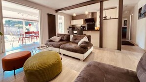 A modern living room with a sofa set, ottoman, and a dining area with red chairs. - Charmante Maison, Piscine, Spacieuse, 5 mn Aix (Aix-en-Provence)